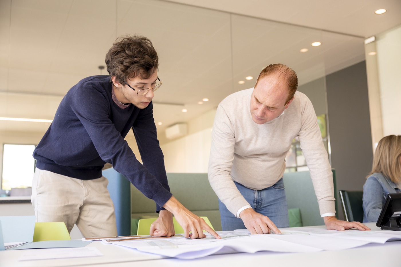 Twee collega’s van Castelein Green Roof overleggen aan een tafel, terwijl ze samen een ontwerpplan bekijken in een moderne kantooromgeving