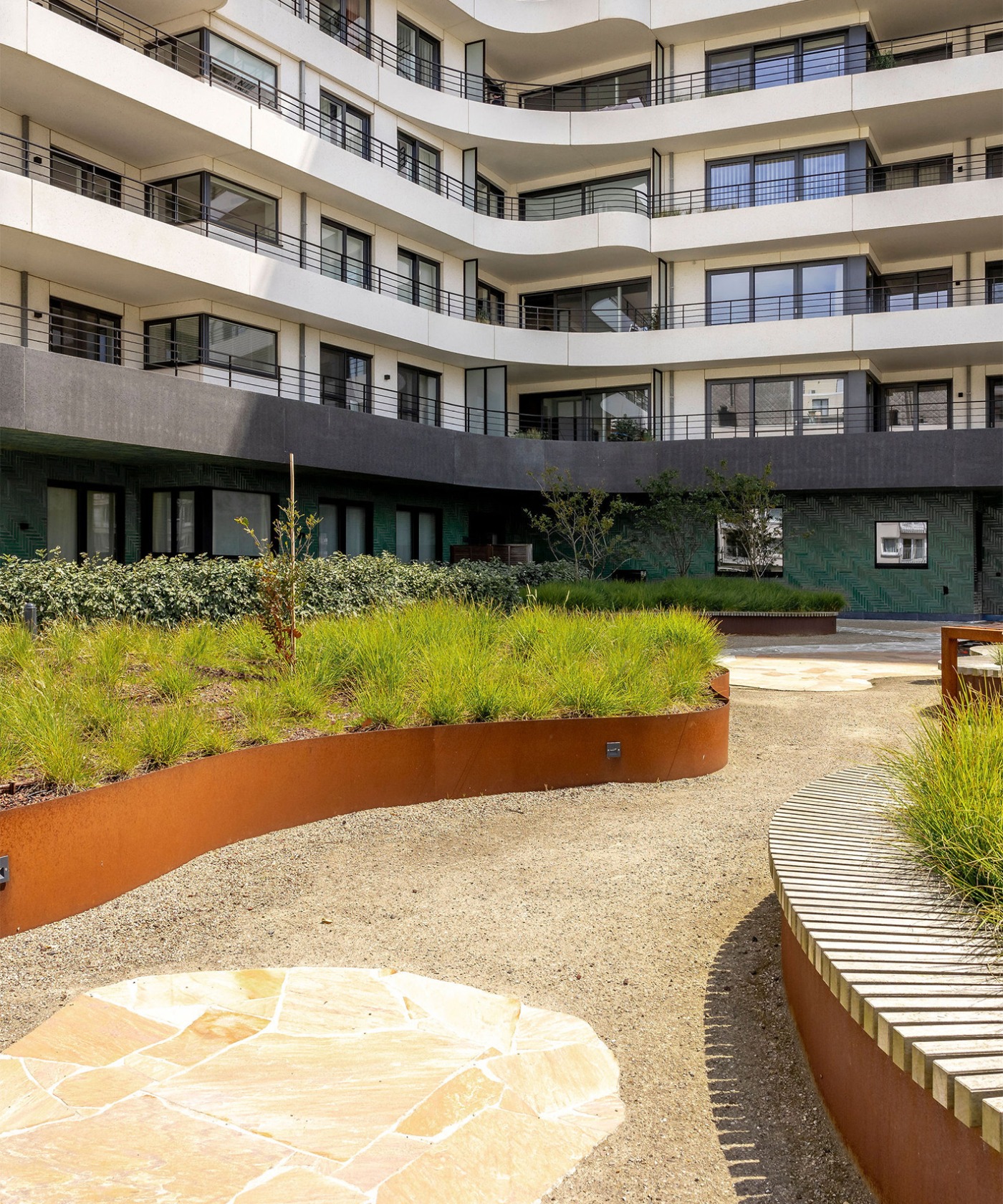 Golvende groene tuin met kleurrijke borders en zitplekken, omgeven door moderne appartementen van The Waves