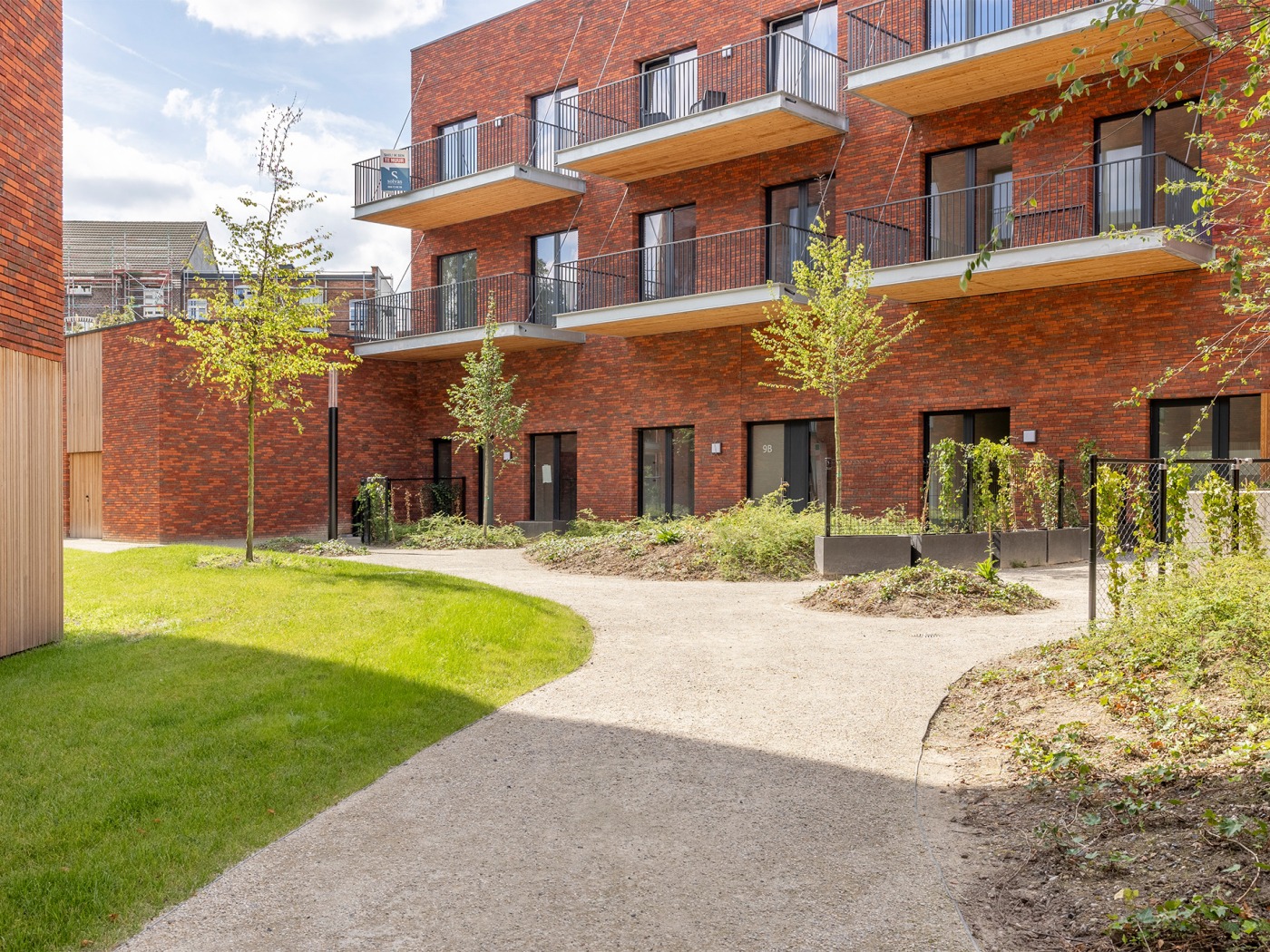 Rode bakstenen appartementen van het Ghandon-project met omliggende wandelpaden en jonge bomen