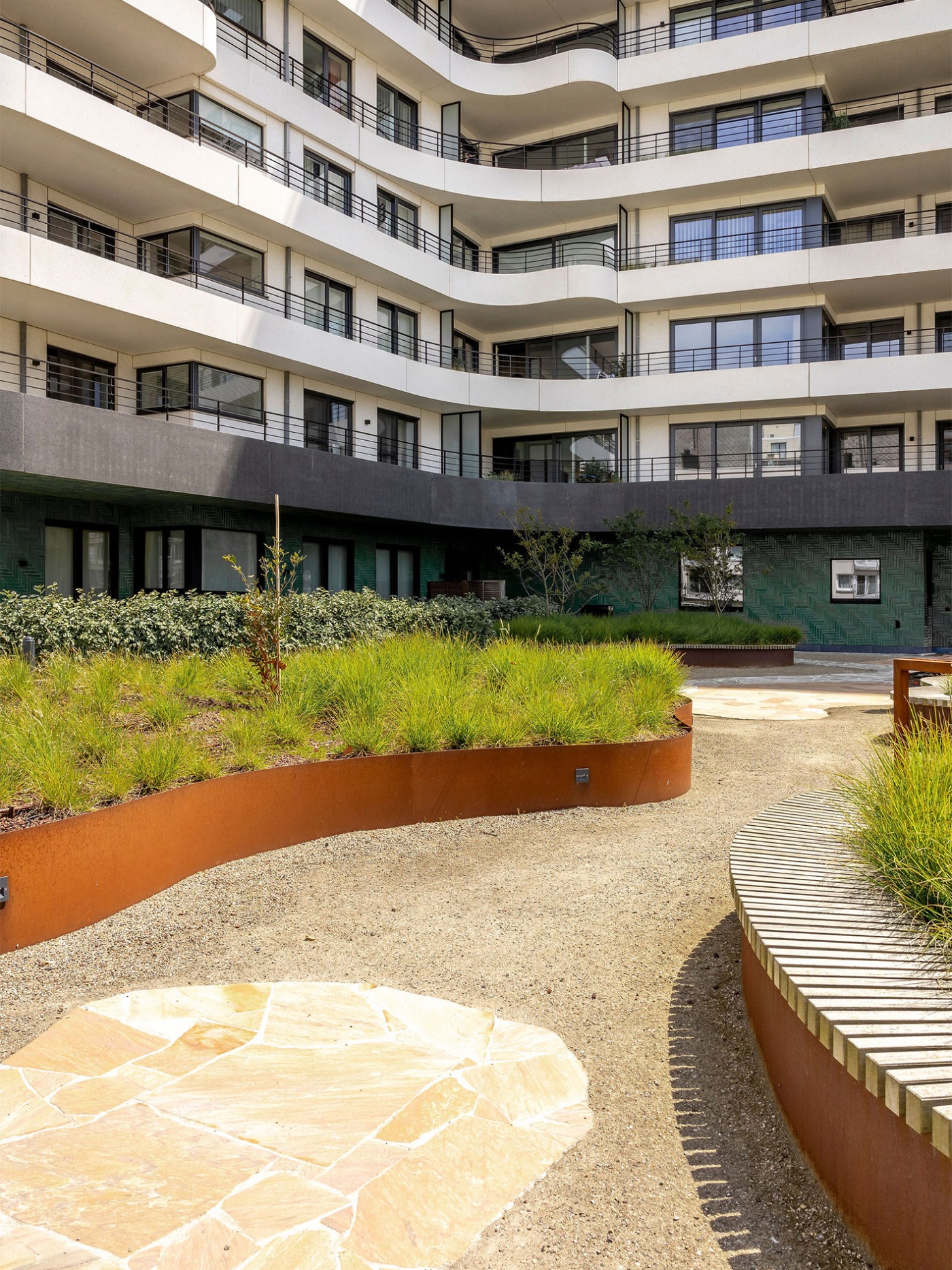 Golvende groene tuin met kleurrijke borders en zitplekken, omgeven door moderne appartementen van The Waves